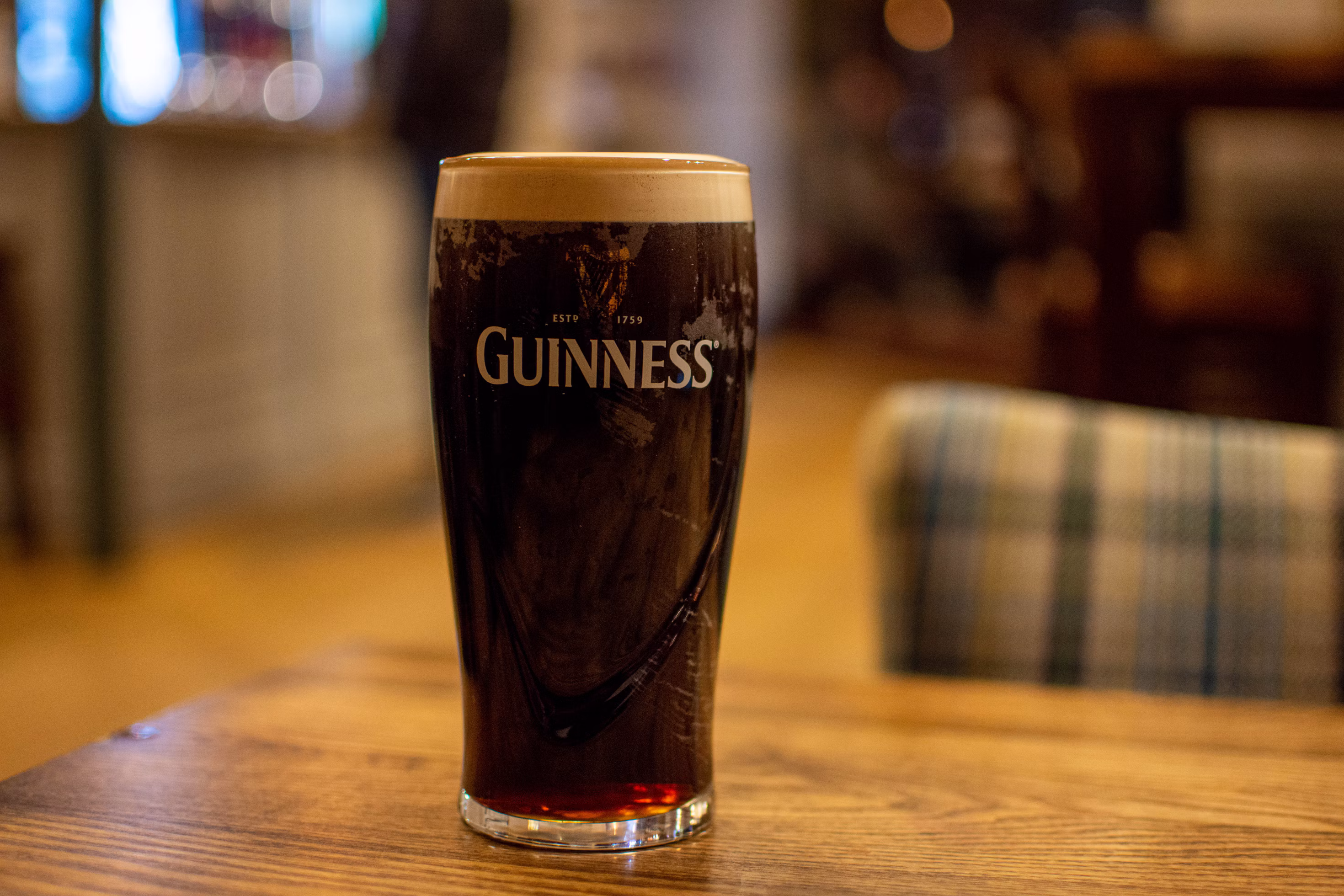 A pint glass of dark stout with a creamy head on a wooden bar